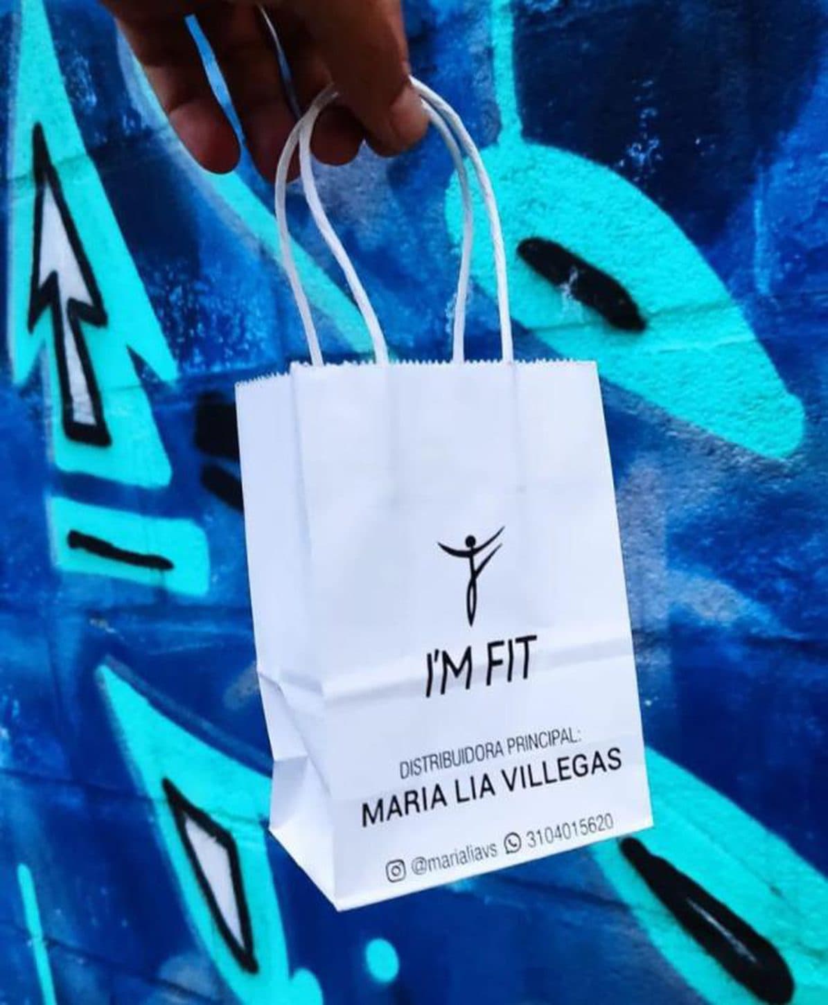 Bolsa de papel personalizada de Bolsas & Empaques Medellín sostenida frente a un muro con grafiti azul